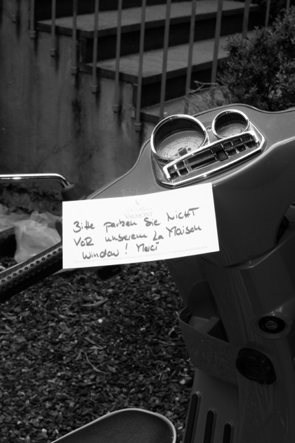 Vespa auf der ein handschriftlicher Zettel am Lenker befestigt ist, schwarz-weiß